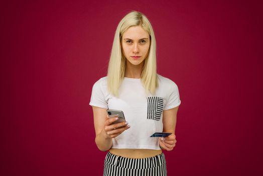 A young woman holds a smartphone and a credit card in her hands. Problems with a bank card, because of blocking or incorrectly entered pincode. Communication with customer support