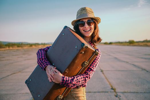 Happy woman traveler embraces a vintage suitcase on road