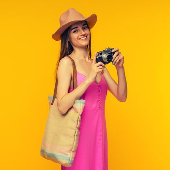 Happy girl in a pink dress and sunglasses holding camera on a yellow background- image