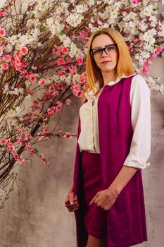 Young girl in a shirt and a vest of fuchsia is standing near the blooming Japanese sakura cherry tree.