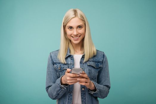 Young beautiful happy woman using smart phone. Isolated on blue background