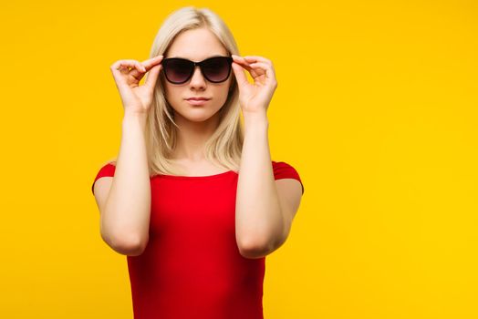 pretty blond lifeguard in red swimsuit and sunglasses on yellow background