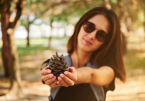 Young woman showing a fir cone in summer park. Eco concept
