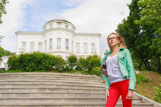 young charming thin woman blonde in leather jacket and red jeans posing near the palace.