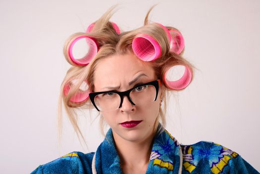 Close-up portraits housewife in a bathrobe and curlers. Looking at the camera with one eyebrow raised