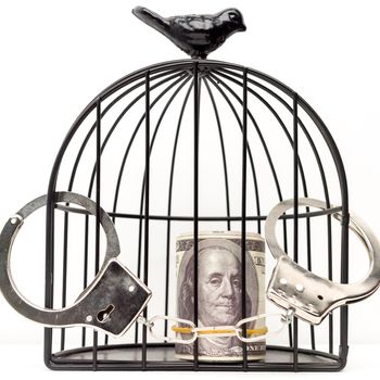 Closed handcuffs hang on the bird cage with money. The concept of imprisonment for a bribe