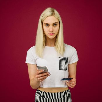 A young woman holds a smartphone and a credit card in her hands. Problems with a bank card, because of blocking or incorrectly entered pincode. Communication with customer support