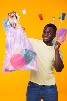 Problem of trash, plastic recycling, pollution and environmental concept - confused man carrying garbage bag on yellow background.