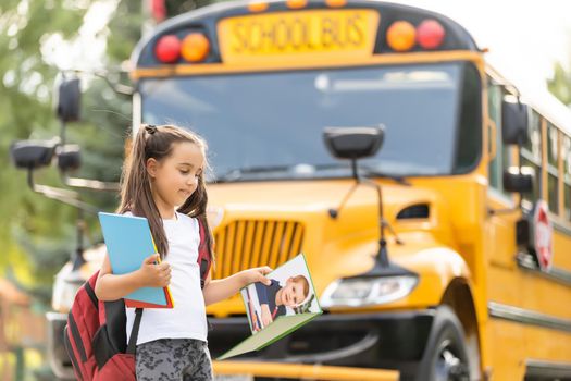 Cute girl with a backpack standing near bus going to school posing to camera pensive close-up