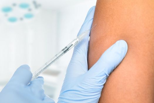 Doctor makes vaccination in the shoulder of patient in a clinic, close-up