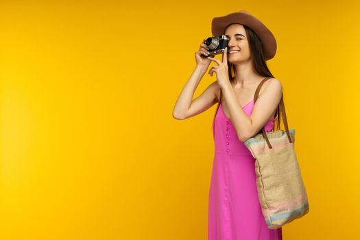 Happy girl in a pink dress and sunglasses holding camera on a yellow background- image