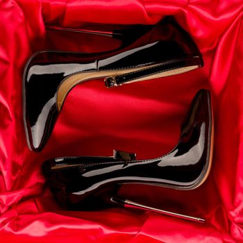 Black fetish shiny patent leather stiletto high heels with ankle strap on red satin background