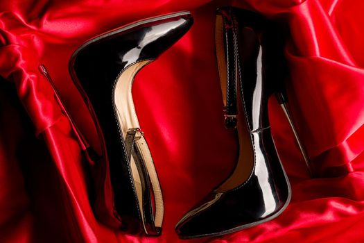 Black fetish shiny patent leather stiletto high heels with ankle strap on red satin background