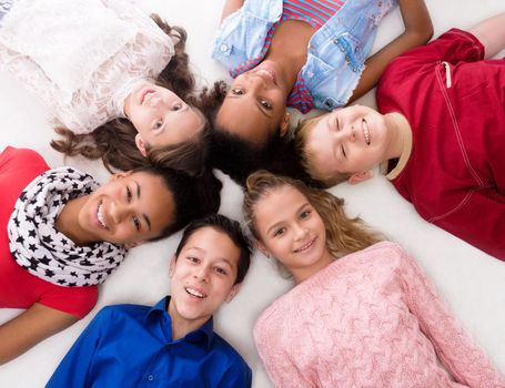 smiling children with different complexion lying head to head on the floor
