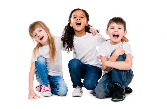 three funny trendy children laugh sitting on the floor isolated on white background