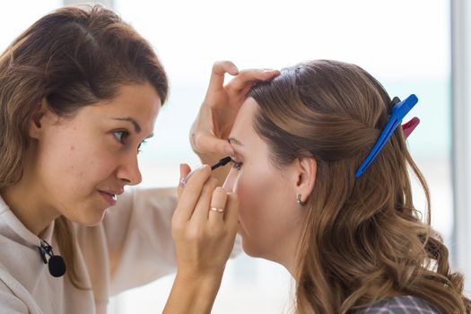 Beauty and cosmetics concept - Makeup artist doing professional make up of young woman.