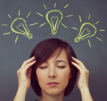 Young woman touches her head on a background of light bulbs, concept of new ideas and concentration