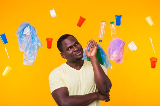World Environment Day, plastic recycling problem and environmental disaster concept - Surprised african american man looking on trash on yellow.