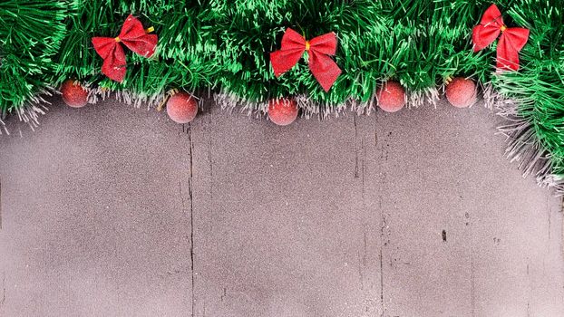 Christmas card. Red balls, tinsel and bow on a snow-covered wooden background with empty spase