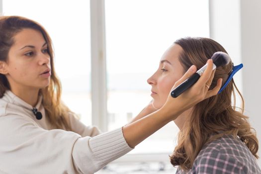 Beauty and cosmetics concept - Makeup artist doing professional make up of young woman.