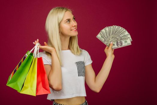 Happy girl in holds one hundred dollars bills and shopping bags on ruby background
