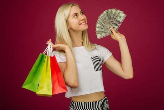Happy girl in holds one hundred dollars bills and shopping bags on ruby background