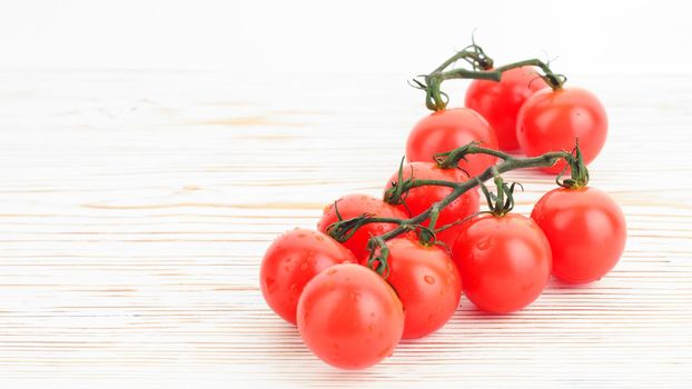 Ripe cherry tomatoes on a twig on a white woden background close up - image