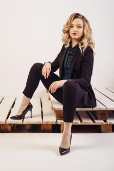 Young attractive business woman in expensive suit and shoes sits on painted pallets.