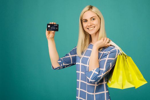 Happy girl in a checkered blouse holds credit card and shopping bags on blue background
