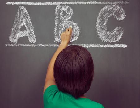 Unrecognizable woman writes ABC alphabet on blackboard, rear view