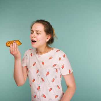 Portrait of pimply teen girl wants to eat eclair cake on blue background