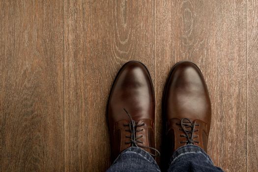 The man wears brown classic shoes on wooden flour. - image