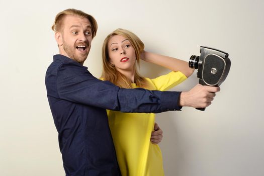 Beautiful couple takes off on an old movie camera standing by the white wall