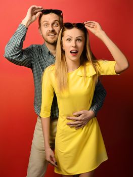Wow. Surprised man and woman in glasses with open mouth an embrace on a red background