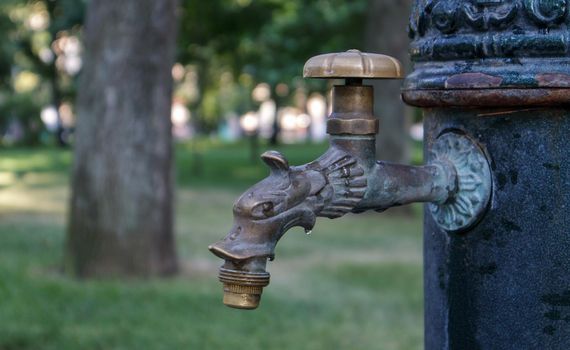 Water well in the park in summer, pumping system, close-up and side view of a beautiful metal bronze faucet. Part of an old iron outdoor tap. Click on the mineral water pump room