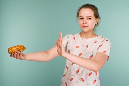Portrait of pimply teen girl hows hands stop on a delicious cake on blue background