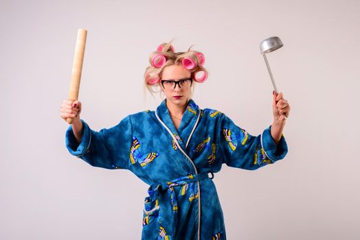 Serious housewife in a dressing gown and curlers with a ladle and battledore.