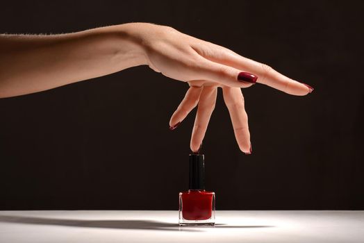 Beauty Hand with red manicure and nail polish bottle.