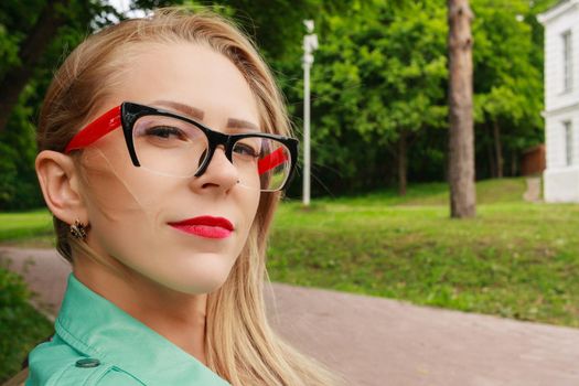 Close up portrait of sensual blonde woman with red lips, stylish glasses for sight. Young lady looks at camera