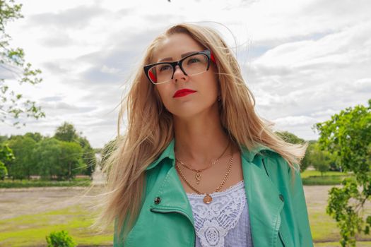 Close up portrait of sensual blonde woman with red lips, stylish glasses for sight. Young lady looks at the sky. The wind blows the hair
