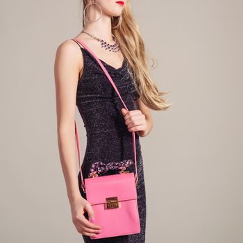 slim trendy woman in evening dress with pink bag in hands and stylish necklace on gray background