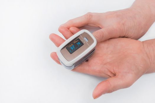 The hands of an elderly woman hold a modern device to measure the saturation of the pulse oximeter on a white background.