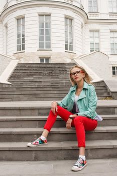 Beautiful stylish girl in jeans and a leather jacket sitting on the stairs near the palace