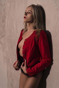 girl in black underwear and a red jacket stands near the gray textured wall