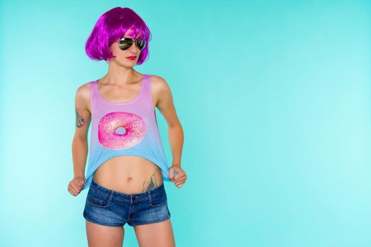 Portrait of young transgender woman in pink wig and sunglasses on blue background - image
