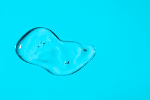 Clear liquid gel smear isolated on light blue background. Top view. Body and face care spa cosmetic concept. Transparent serum or hyaluronic acid texture. Banner with copy space.
