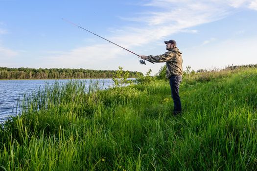 bearded man in a blue baseball cap on the river throws a spinning fishing