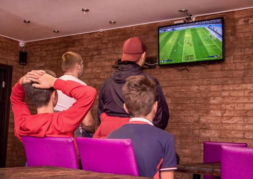 A company of young people indoors playing video games and looking at the screen.