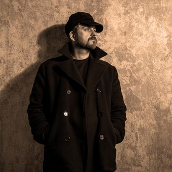 man in vintage cap and coat standing near old wall. black and white photo