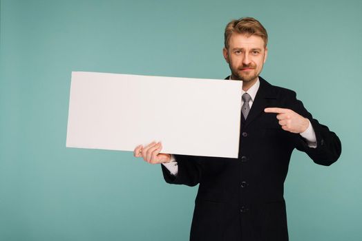 Happy smiling young business man points finger blank signboard, on blue background